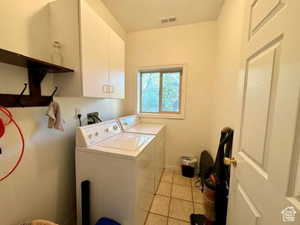 Washroom with visible vents, light tile patterned floors, baseboards, separate washer and dryer, and cabinet space