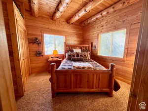Carpeted bedroom featuring wooden ceiling, wood walls, multiple windows, and beamed ceiling