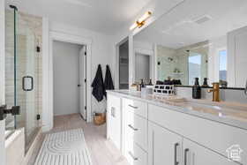 Full bath with a sink, wood finished floors, a stall shower, double vanity, and visible vents