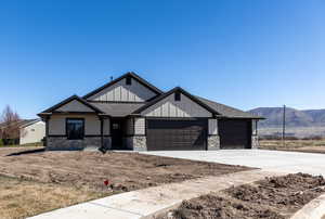 View of front of house with a mountain view, stone siding, concrete driveway, a garage, and board and batten siding