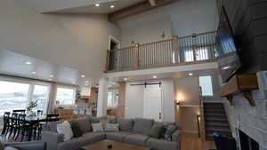 Living area with high vaulted ceiling, a barn door, wood finished floors, beamed ceiling, and recessed lighting