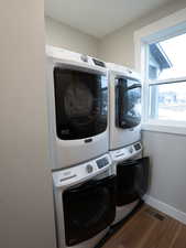 Laundry area featuring stacked washer and dryer, visible vents, baseboards, wood finished floors, and laundry area