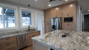 Kitchen featuring decorative light fixtures, light stone countertops, stainless steel appliances, and a sink