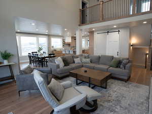 Living room featuring a barn door, wood finished floors, a towering ceiling, baseboards, and recessed lighting