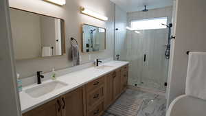 Full bath featuring marble finish floor, a sink, a shower stall, and double vanity
