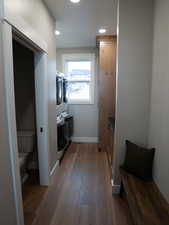 Hallway featuring baseboards, wood finished floors, stacked washing maching and dryer, and recessed lighting