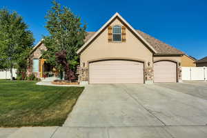 View of front of house with driveway, stone siding, a front lawn, and stucco siding