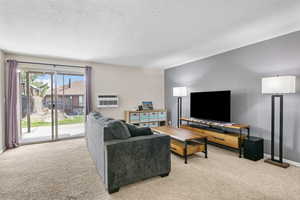 Living room featuring baseboards, carpet floors, a sliding glass door opening onto a patio, and a wall unit AC.