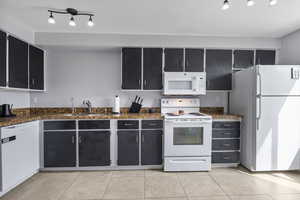 Kitchen with light tile patterned flooring, dark cabinetry, a sink, and white appliances