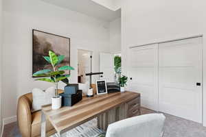 Carpeted home office featuring a towering ceiling