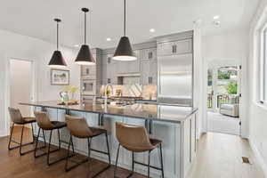 Kitchen with gray cabinets, light wood-style flooring, dark stone countertops, a large island, and a kitchen bar