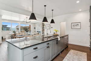 Kitchen with recessed lighting, dark wood-style flooring, open floor plan, dark stone countertops, and a kitchen island with sink