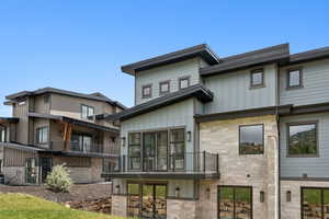 Back of house with a balcony, board and batten siding, and stone siding