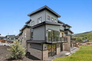 Back of property featuring board and batten siding, stone siding, and a balcony
