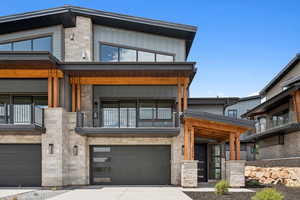 View of front of house featuring stone siding, concrete driveway, a garage, and a balcony