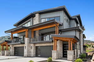 Contemporary home with stone siding, a balcony, an attached garage, and concrete driveway