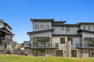 Back of house with stone siding, a balcony, and board and batten siding