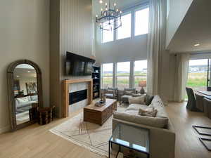 Living room with a tiled fireplace, a high ceiling, a wealth of natural light, and light wood-style floors