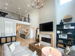 Living room with light wood finished floors, a tiled fireplace, a towering ceiling, and recessed lighting