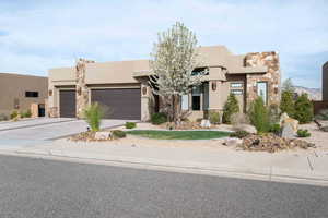 Pueblo revival-style home with an attached garage, driveway, stone siding, and stucco siding