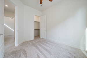 Unfurnished bedroom featuring a spacious closet, a ceiling fan, baseboards, and light carpet