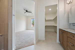 Interior space with a walk in closet, vanity, ceiling fan, baseboards, and tile patterned flooring