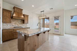 Kitchen featuring a sink, a center island with sink, visible vents, custom exhaust hood, and backsplash