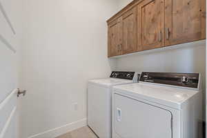 Laundry area featuring separate washer and dryer, baseboards, light tile patterned floors, and cabinet space