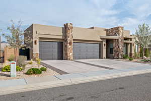 View of front facade with stucco siding, an attached garage, driveway, and stone siding