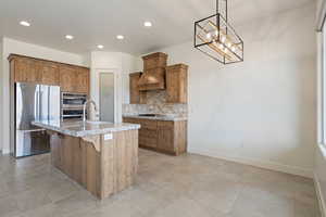 Kitchen with stainless steel appliances, a sink, backsplash, light stone counters, and premium range hood