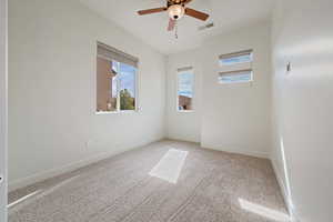 Unfurnished room featuring a ceiling fan, carpet floors, a healthy amount of sunlight, and visible vents