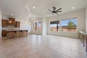 Kitchen with ceiling fan with notable chandelier, decorative backsplash, brown cabinets, custom range hood, and recessed lighting