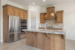 Kitchen with recessed lighting, a kitchen bar, decorative backsplash, appliances with stainless steel finishes, and premium range hood