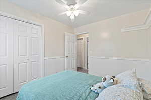 Bedroom with a closet, carpet flooring, a wainscoted wall, and ceiling fan