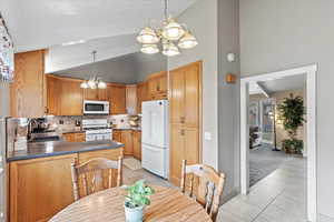 Kitchen featuring a sink, decorative backsplash, white appliances, light tile patterned floors, and an inviting chandelier