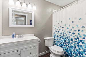 Bathroom featuring toilet, a textured wall, wood finished floors, and baseboards