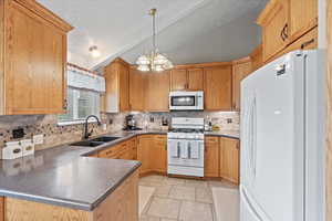 Kitchen featuring a sink, vaulted ceiling, an inviting chandelier, decorative backsplash, and white appliances
