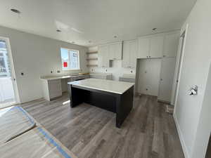 Kitchen featuring a textured ceiling, wood finished floors, a kitchen island, and white cabinets