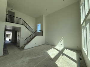 Unfurnished living room featuring plenty of natural light, baseboards, a high ceiling, and stairway