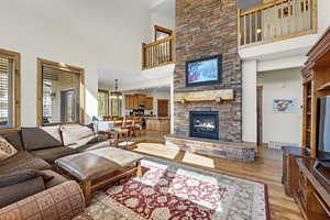 Living room featuring visible vents, a high ceiling, a stone fireplace, a chandelier, and light wood-style floors