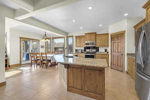 Kitchen with a notable chandelier, an island with sink, light tile patterned floors, appliances with stainless steel finishes, and a sink