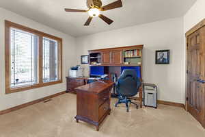 Office area featuring light carpet, baseboards, a ceiling fan, and visible vents