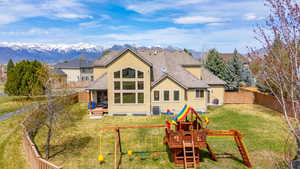 Rear view of house with a mountain view, a fenced backyard, a playground, and stucco siding