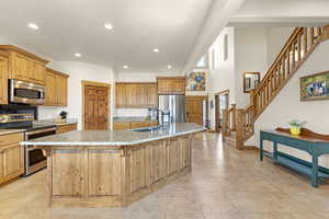 Kitchen with light stone counters, recessed lighting, a center island with sink, stainless steel appliances, and a sink