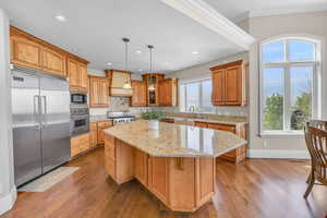Kitchen with a center island, custom exhaust hood, built in appliances, baseboards, and ornamental molding