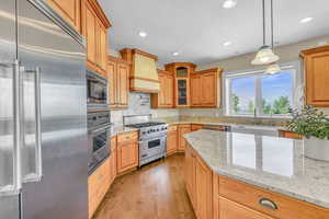 Kitchen featuring a sink, built in appliances, glass insert cabinets, wood finished floors, and light stone counters