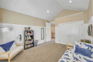Bedroom with high vaulted ceiling, a decorative wall, a closet, wainscoting, and light carpet