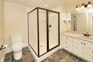 Bathroom with a shower stall, toilet, stone tile flooring, and recessed lighting