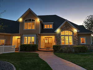 Craftsman-style home featuring roof with shingles, stone siding, and a front lawn