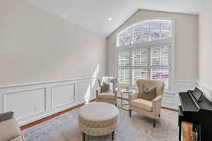 Sitting room featuring vaulted ceiling, light wood-type flooring, a decorative wall, and a wainscoted wall